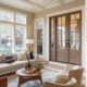 The image depicts a modern, family-oriented living room with large windows allowing natural light to flood the space, a sleek new door, and elegant hardwood flooring.