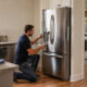 Homeowner cleaning a refrigerator in a modern kitchen with a washer and dryer visible in the adjacent laundry area.